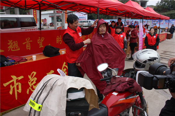 梧州市總工會的黨員義工們在市東出口春運服務站助力“摩托大軍”平安返鄉(xiāng)，幫助他們檢查車輛和行李，穿上雨衣。--黃賀峰攝.j